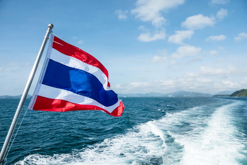 Dynamic view of the Thai flag waving aboard a boat, sailing through a vast seascape.